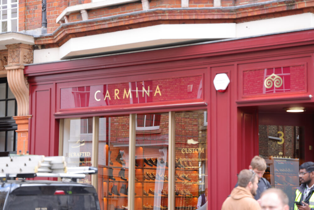 A storefront with the name "CARMINA" in gold lettering on a deep red background, showcasing a variety of shoes in the display.