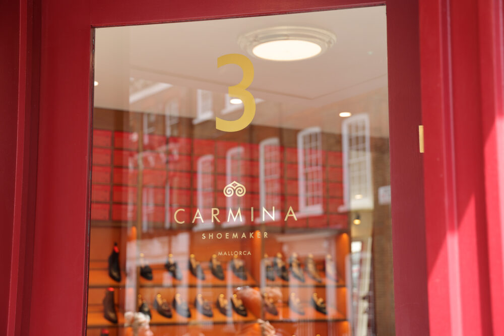 A glass door displays the gold lettering "3 CARMINA SHOEMAKER MALLORCA" with a red background.