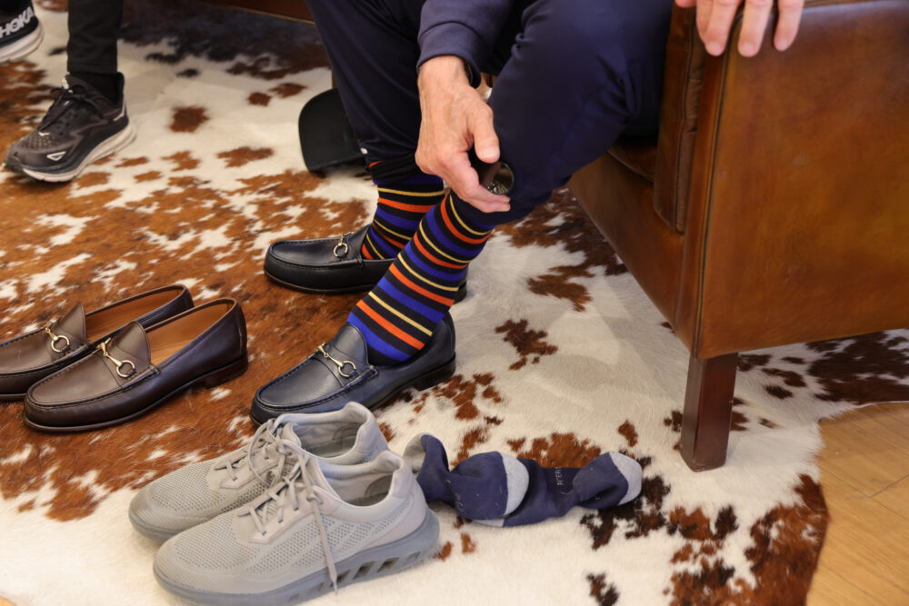 A person wearing colorful striped socks and dark loafers adjusts their sock while sitting on a brown leather chair.