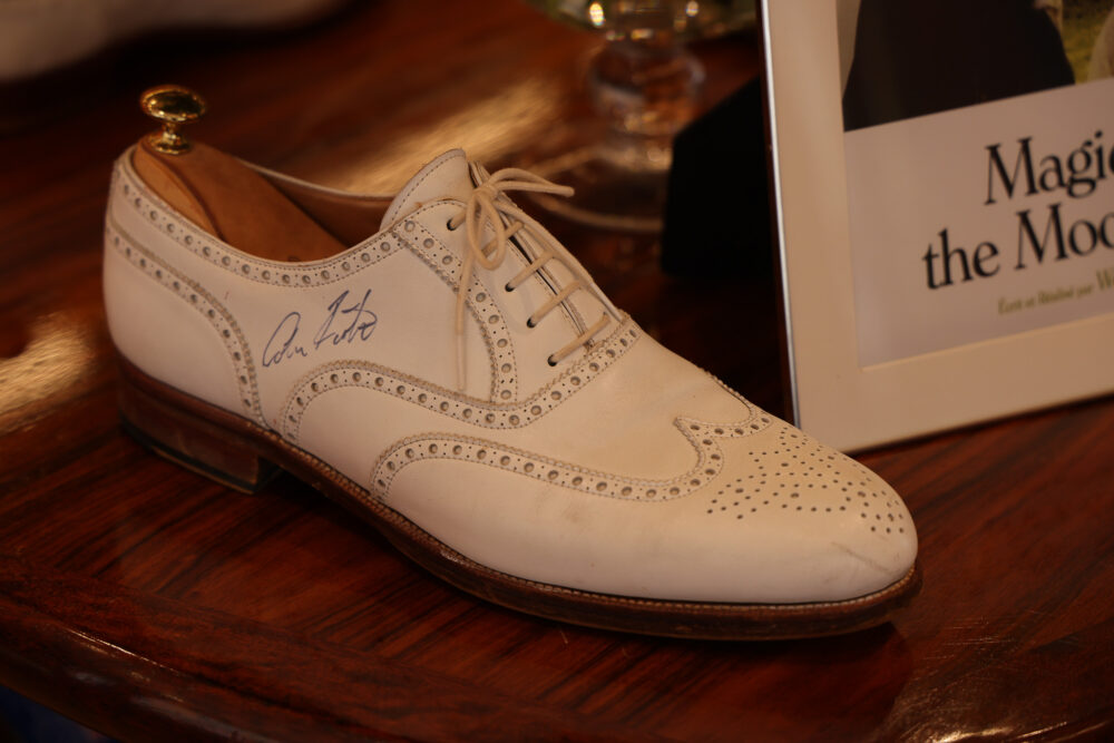 A white leather dress shoe with decorative perforations and a signature on the side.