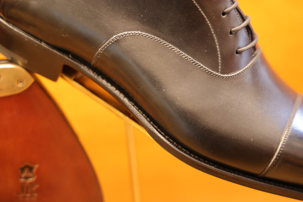 A close-up of a polished black leather dress shoe with intricate stitching details.