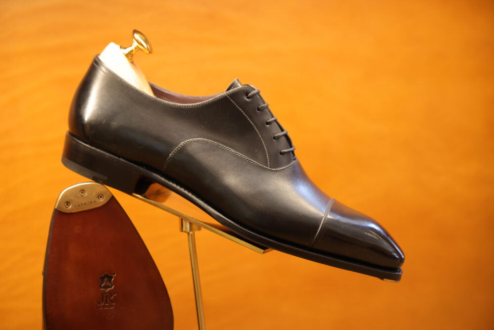 A polished black leather dress shoe with a gold shoehorn and a wooden shoe tree inside.