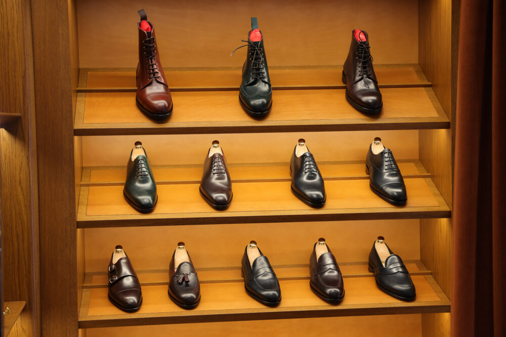 A display of assorted men's leather shoes in various shades of brown and green, arranged on wooden shelves.