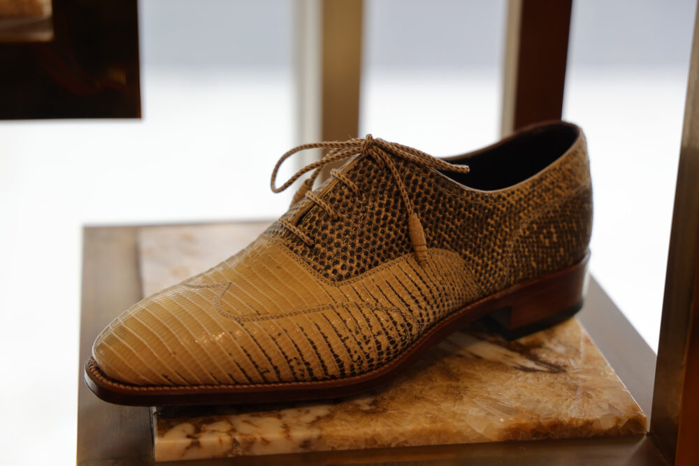 A stylish men's shoe made of beige crocodile and snakeskin leather with a low heel and lace-up design.