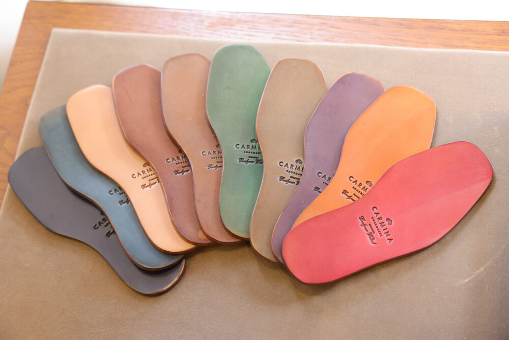A collection of leather shoe insoles in various colors, including brown, green, and red, with the brand name "Carmina" embossed on each.
