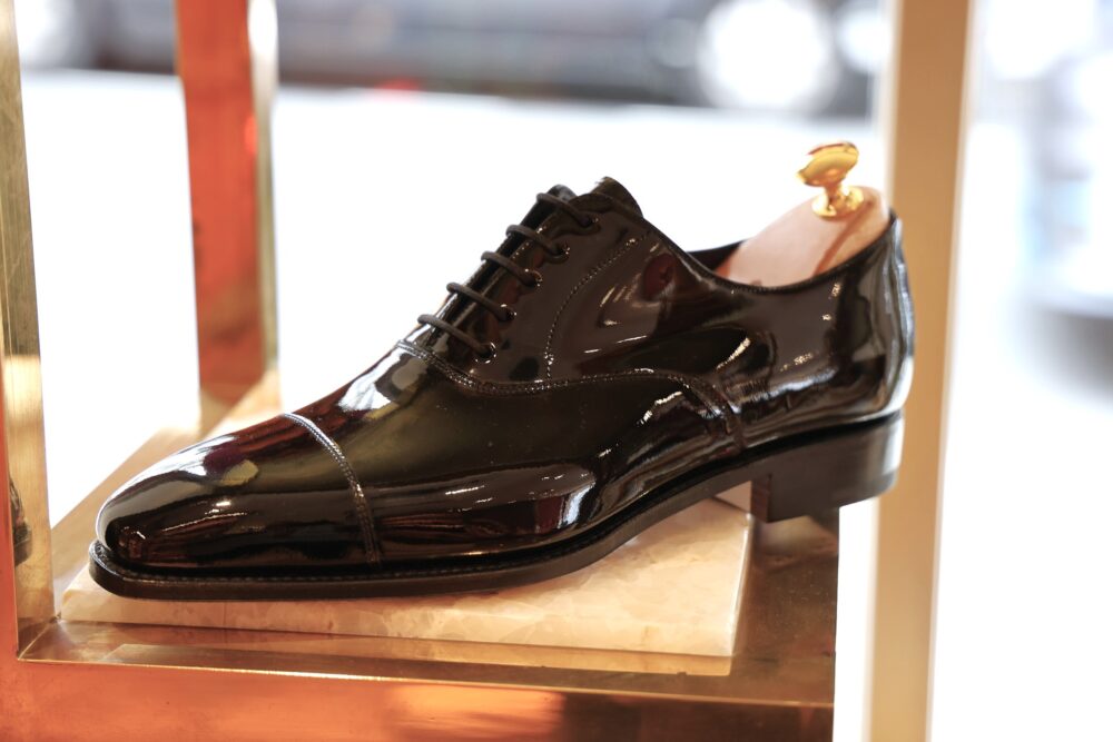 A polished black dress shoe with laces and a shoe tree displayed on a marble base.