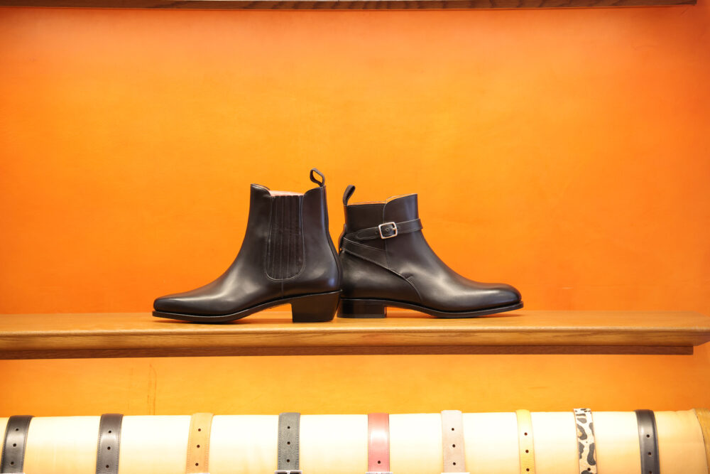 Two black leather ankle boots with a low heel are displayed on a wooden shelf.