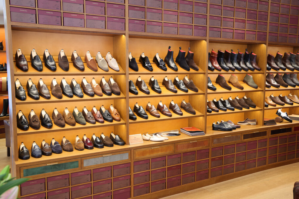 A display of various styles of leather shoes in shades of brown and black arranged on wooden shelves.