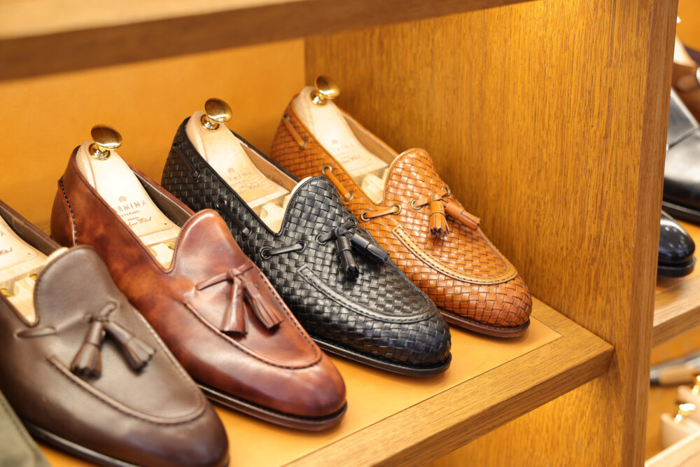 A display of loafers in various shades of brown and black leather, featuring woven textures and tassel details.