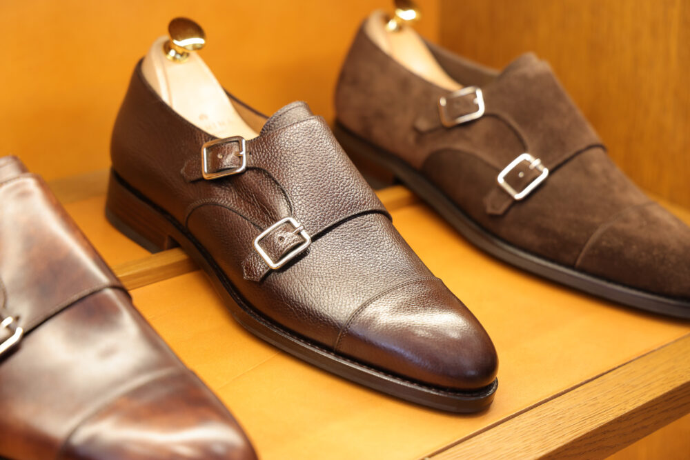 A pair of brown leather dress shoes with double buckles, one in smooth leather and the other in suede.