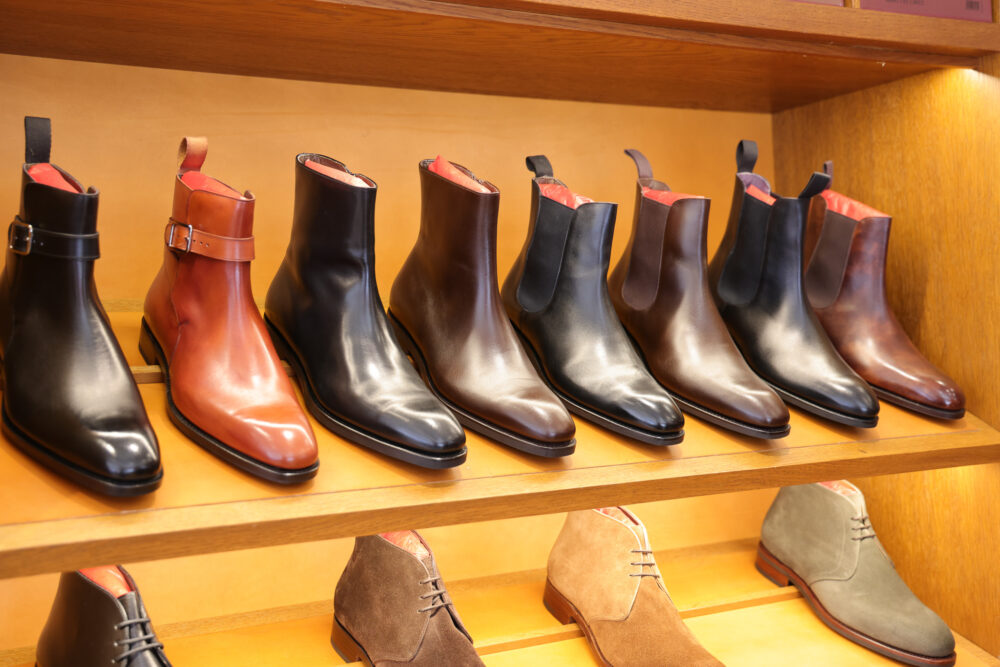 A variety of leather boots in black, brown, and tan, displayed on wooden shelves.
