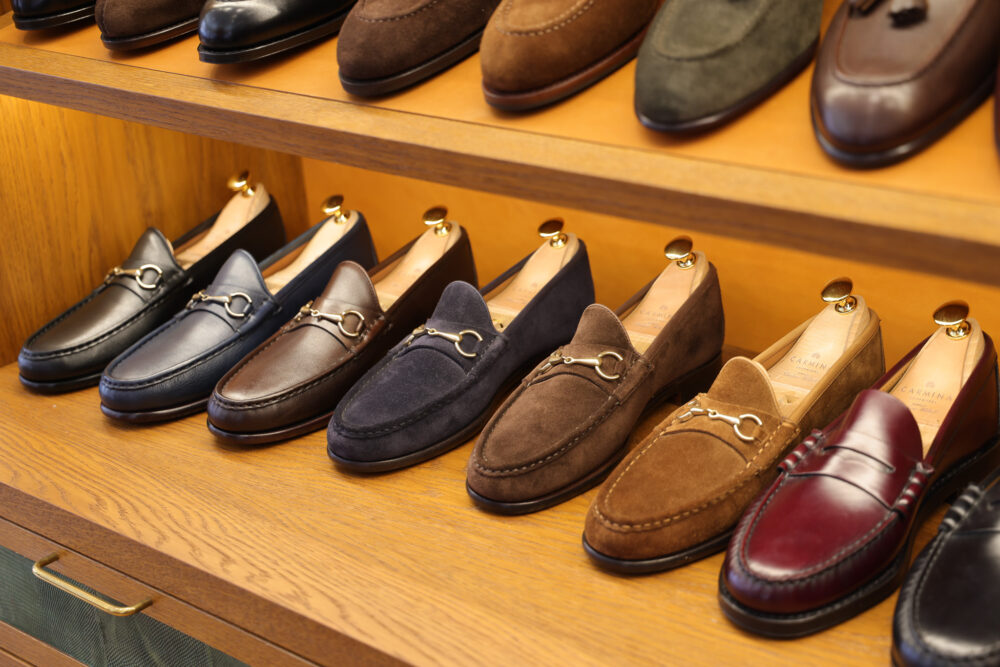 A display of leather loafers in black, brown, navy, and burgundy, featuring gold accents.