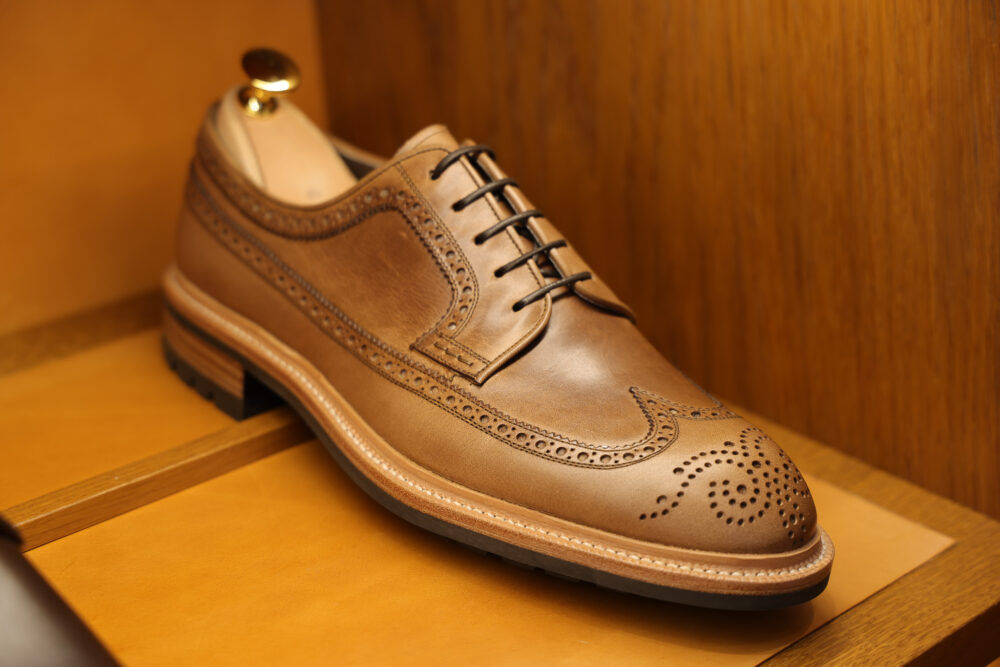 A brown leather dress shoe with decorative perforations and black laces.