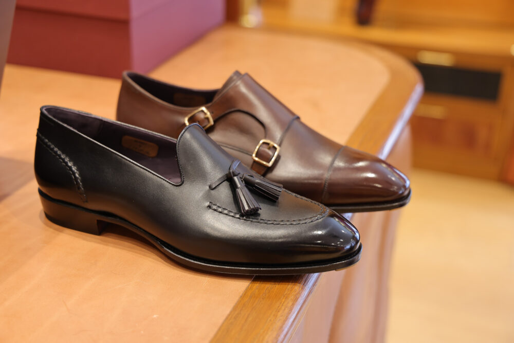 A black leather loafer with tassels is positioned next to a brown leather dress shoe with a buckle.