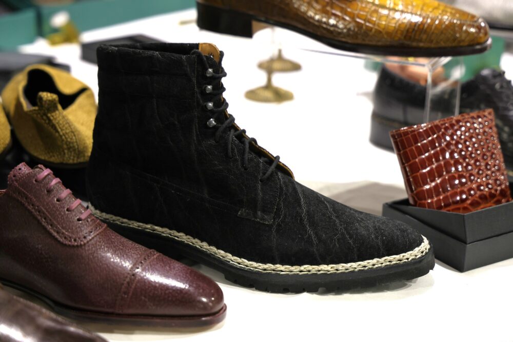 A pair of black leather boots with a textured finish and a braided sole, surrounded by various other shoes.