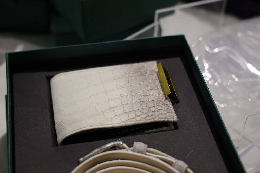 A white crocodile-patterned wallet with a gold clasp sits in a black box.