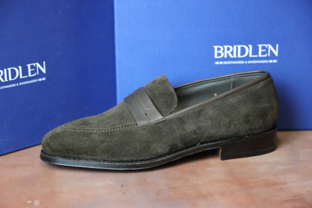 A dark green suede loafer shoe with a smooth leather band across the top.