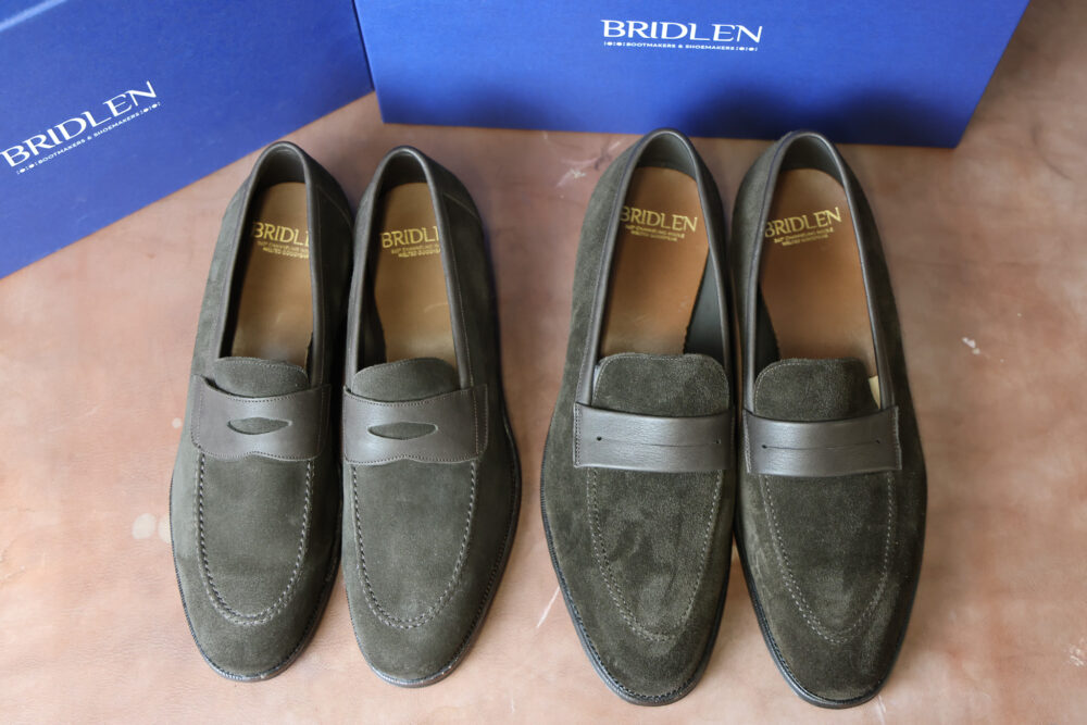 A pair of olive green suede loafers with brown leather accents.