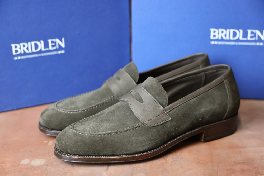 A pair of dark green suede loafers with leather accents and a low heel.