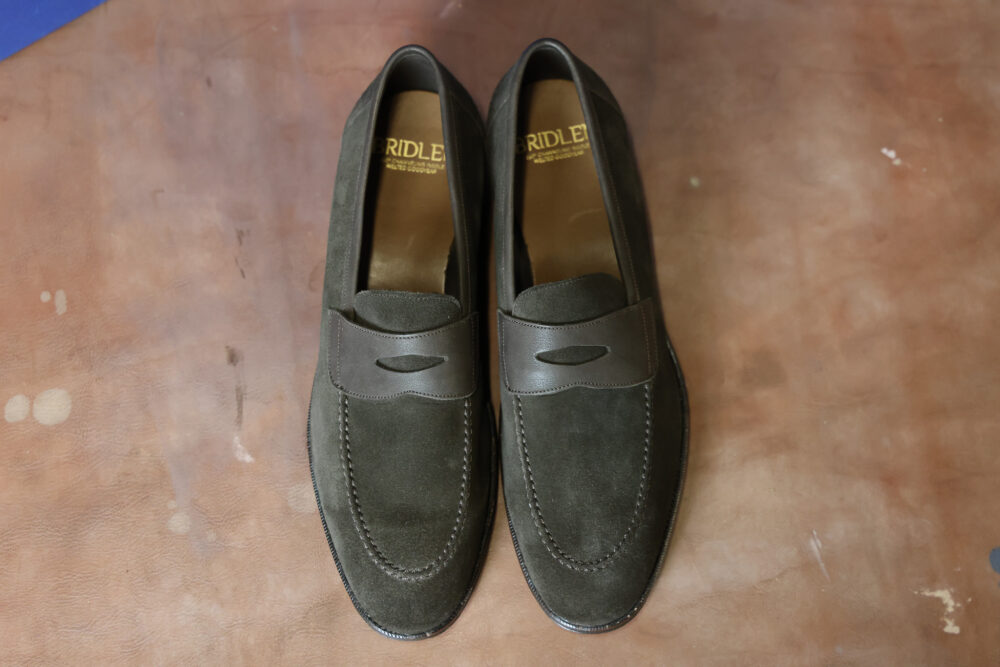 A pair of dark green suede loafers with a brown leather accent.