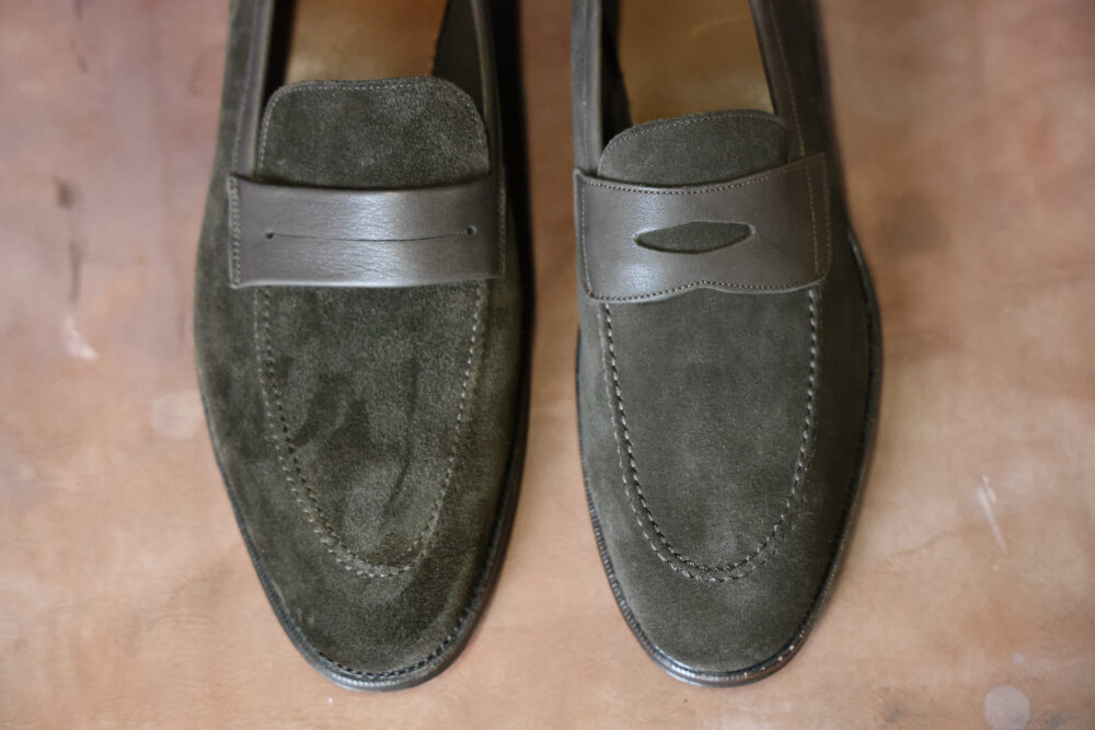 A pair of dark green suede loafers with leather accents.