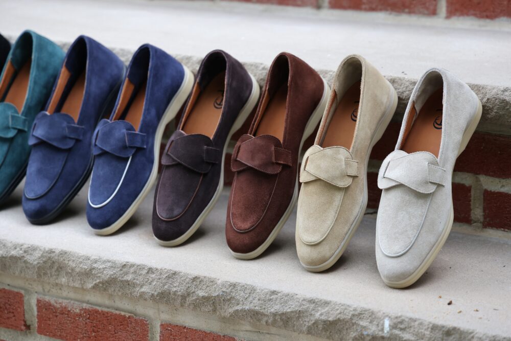 A row of loafers in varying colors including teal, navy, dark brown, light brown, and beige, all made of suede.
