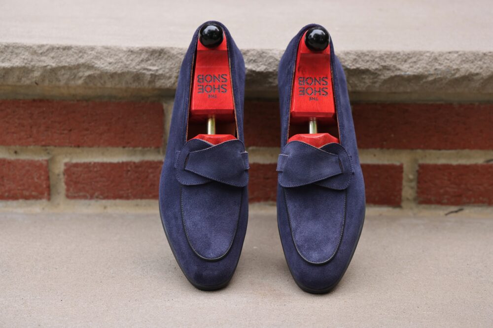 A pair of navy blue suede loafers with red insoles and shoe trees inside.