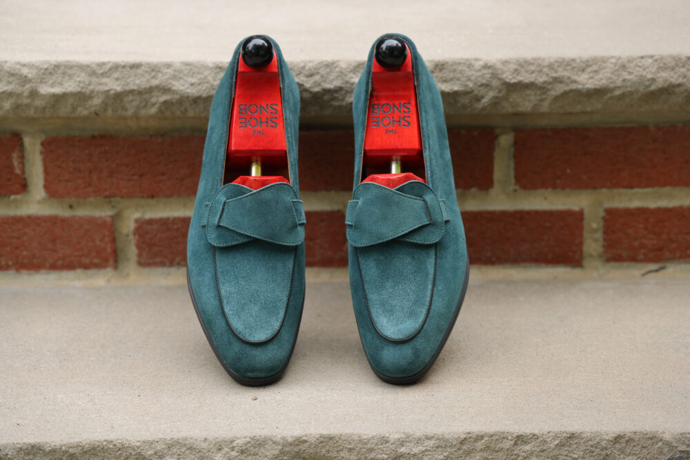A pair of teal suede loafers with red insoles and shoe trees.