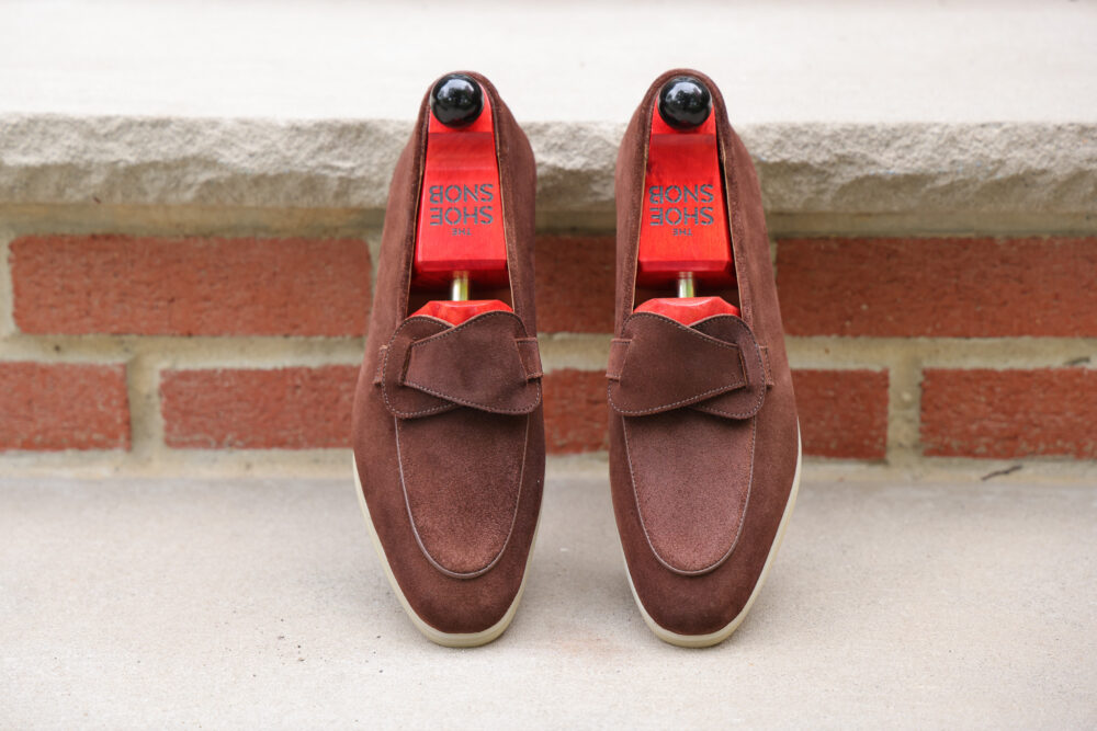 A pair of brown suede loafers with a bow detail and shoe trees inside.