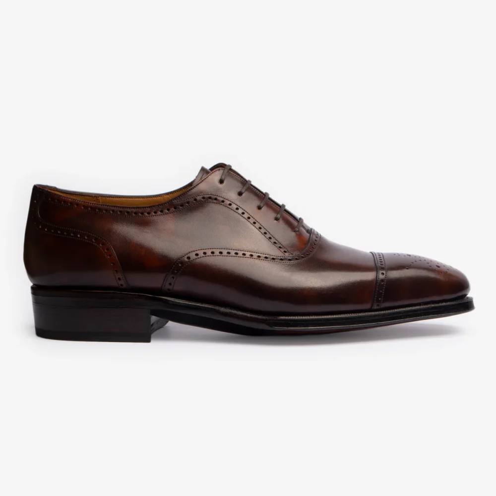 A polished brown leather dress shoe with a cap toe and decorative perforations.