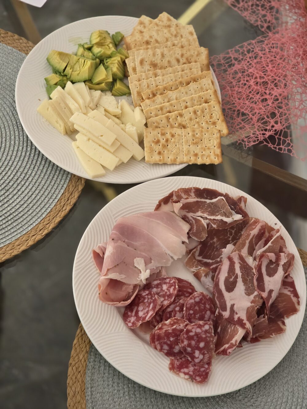 A plate with sliced cheeses, crackers, avocado, and assorted cured meats.