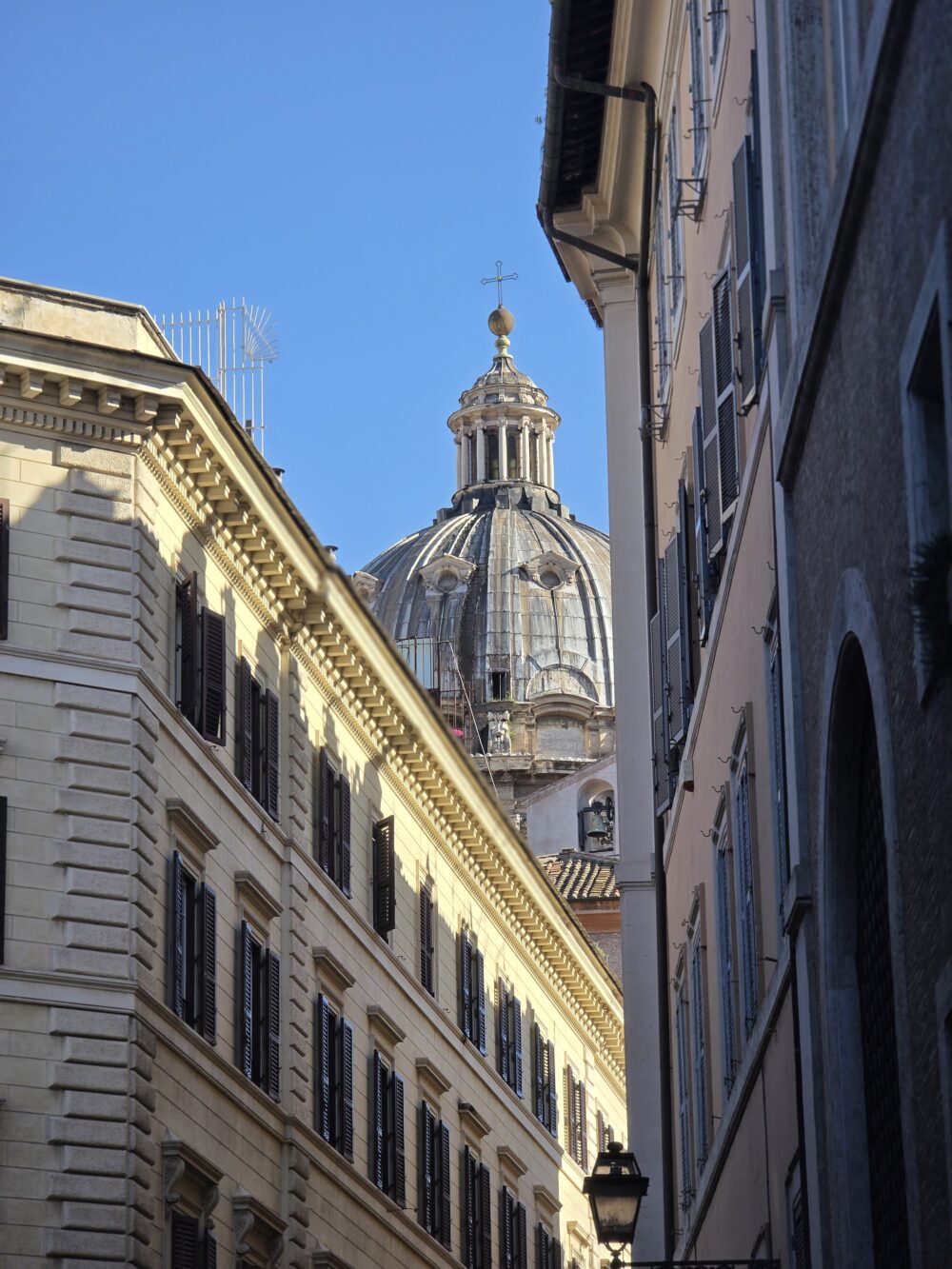 A dome with a cross and gold orb is visible between two buildings with light-colored façades.