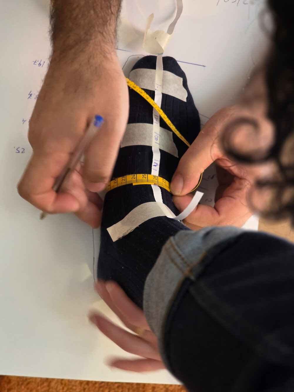 A person measures a socked foot using a tape measure and a pen on a sheet of paper.
