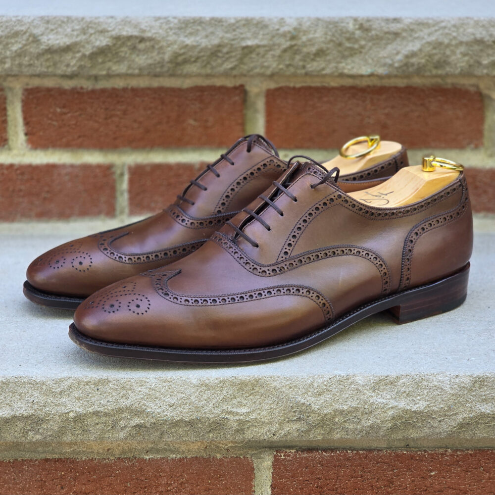 A pair of polished brown leather dress shoes with decorative broguing and shoe trees inserted.