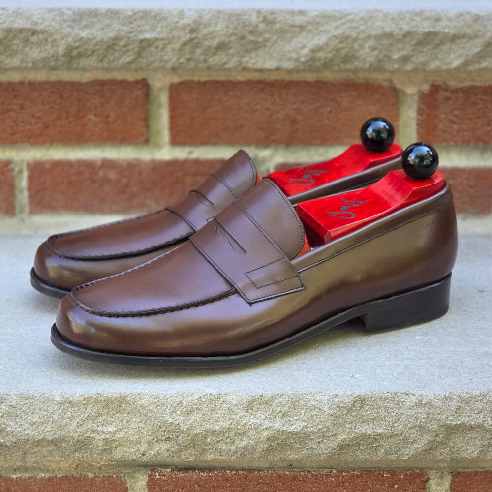 A pair of brown leather loafers with red shoe trees inserted.