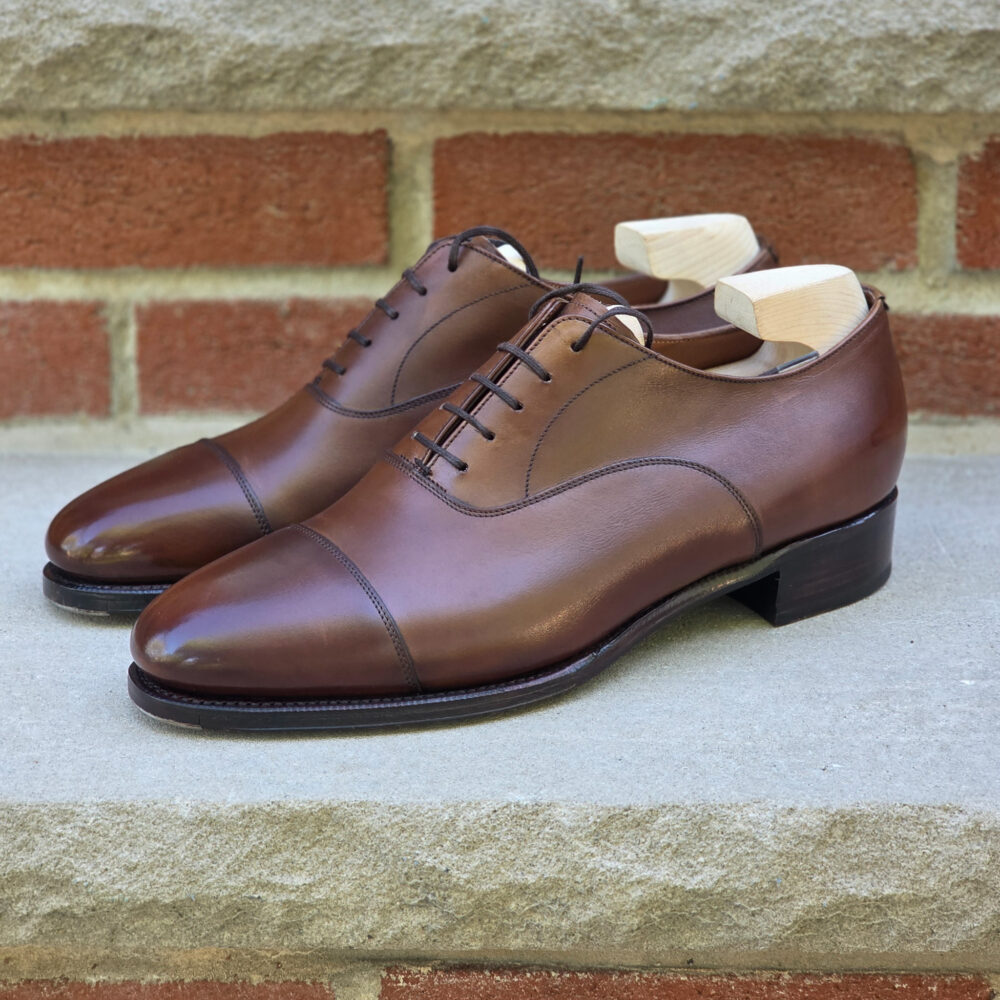 A pair of polished brown leather dress shoes with wooden shoe trees inserted.