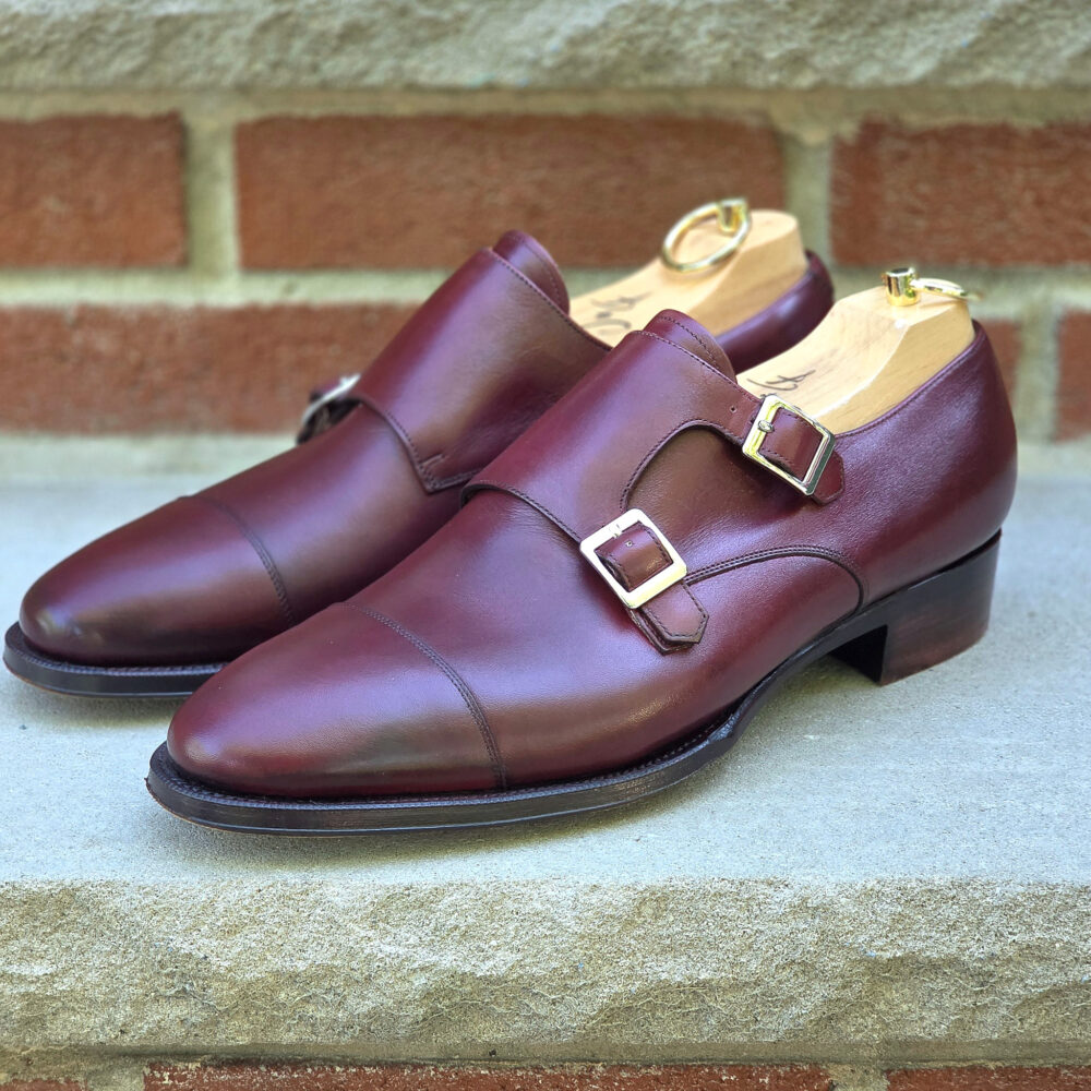 A pair of burgundy leather double monk strap shoes with gold buckles.