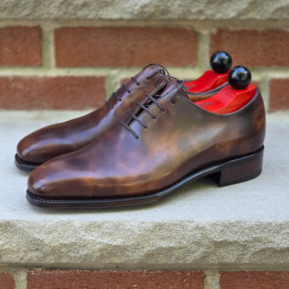 A pair of polished brown leather dress shoes with red insoles and black shoe trees.