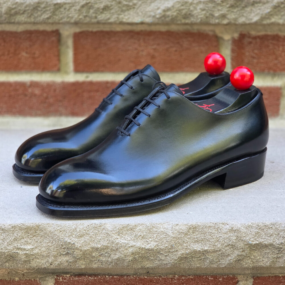 A pair of shiny black leather dress shoes with red accents on the heel.