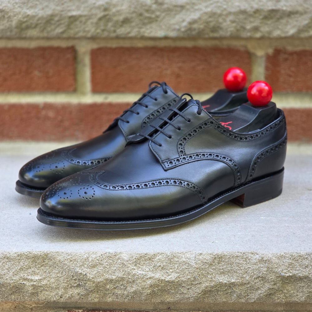 A pair of black leather dress shoes with decorative perforations and red shoe trees inserted.