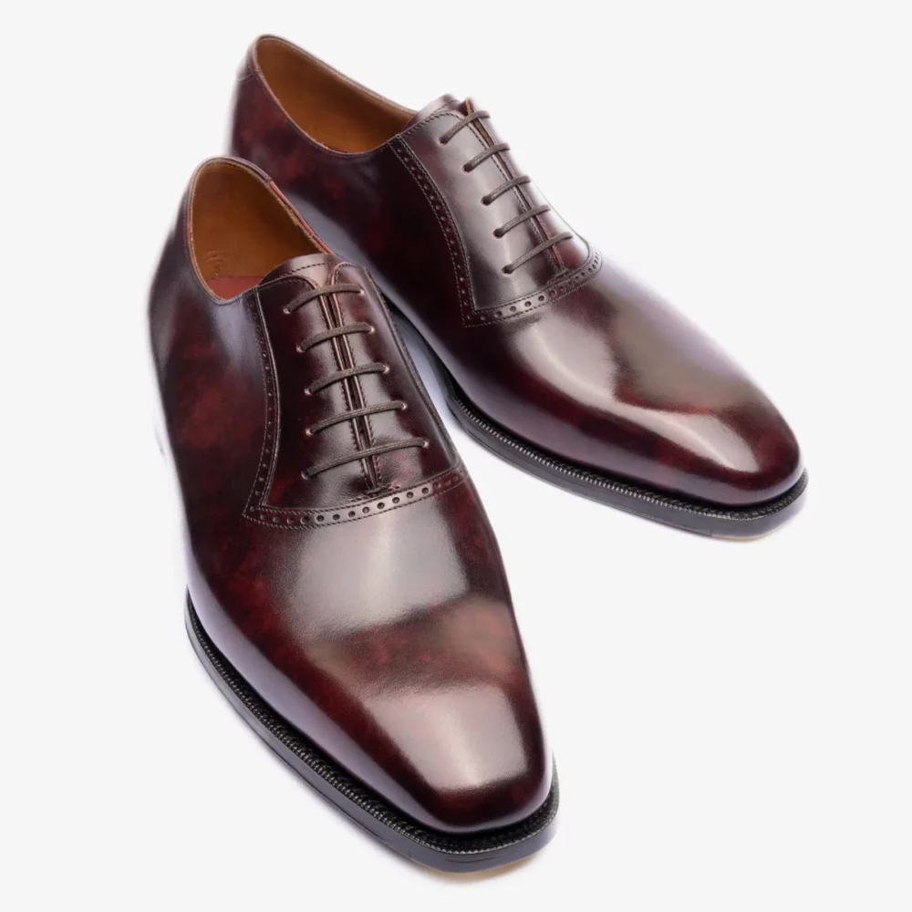 A pair of polished burgundy leather dress shoes with a pointed toe and six eyelets for laces.