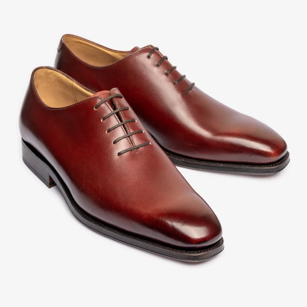 A pair of polished burgundy leather dress shoes with a pointed toe and six eyelets for laces.