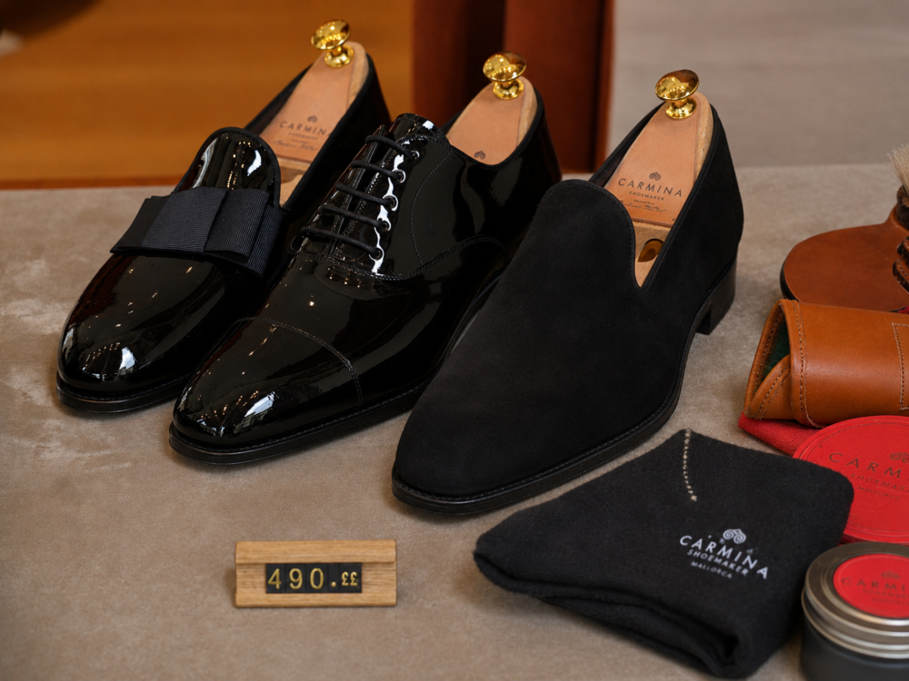 Three pairs of shoes are displayed: a glossy black patent leather pair with a bow, a black leather pair with laces, and a black suede slip-on, with a price tag of 490.33.