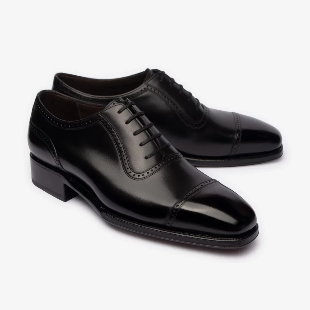 A pair of polished black leather dress shoes with a cap toe and decorative stitching.