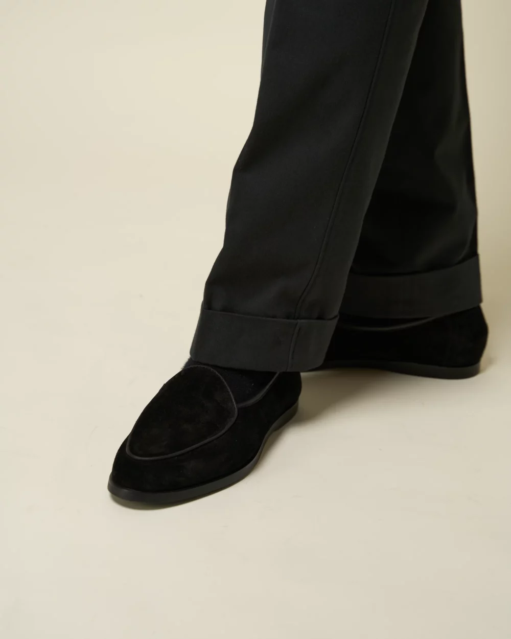 A close-up of a black suede shoe paired with black tailored pants.