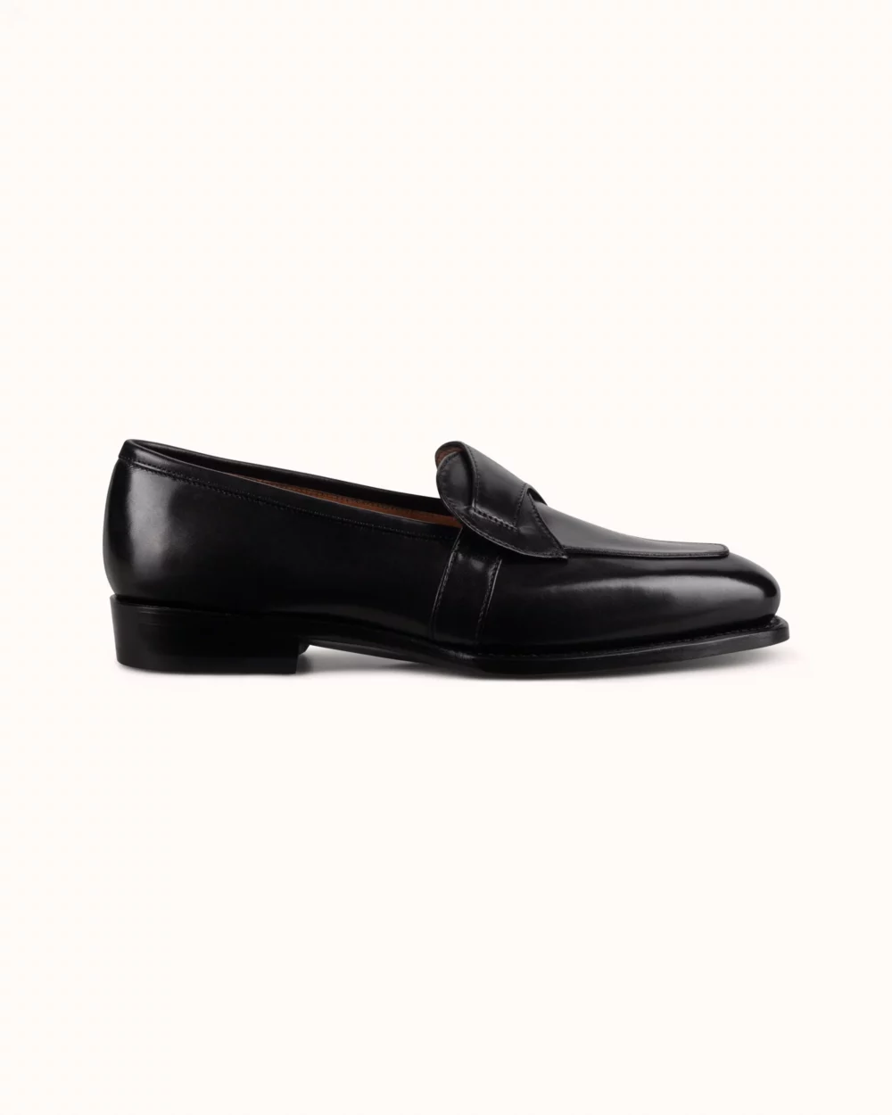 A black leather loafer with a low heel and a stitched detail on the front.