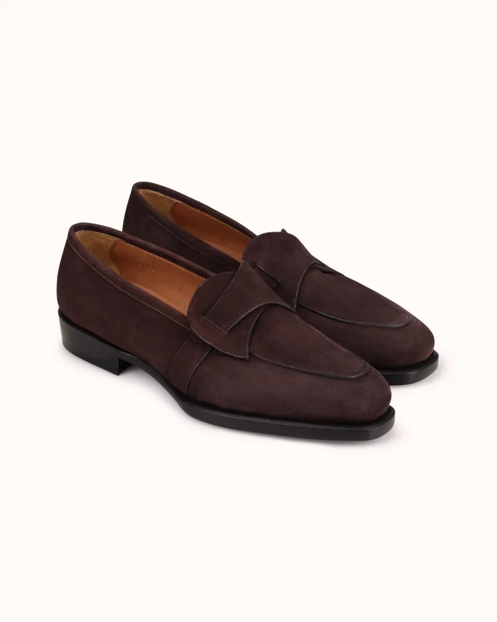 Brown suede loafers with a rounded toe and a decorative strap detail.
