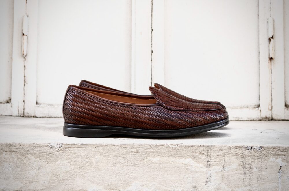 A pair of brown woven loafers with a smooth black sole.