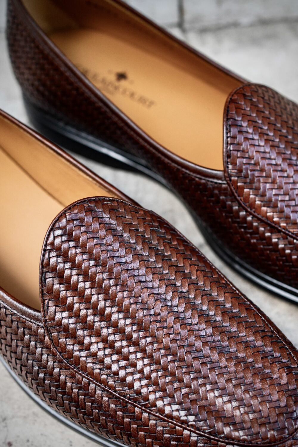 A close-up of woven brown leather loafers with a smooth interior.