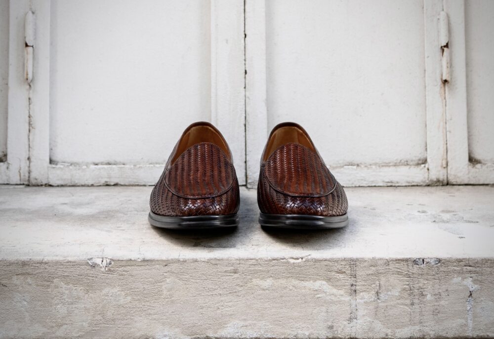 A pair of brown woven leather loafers positioned toe-to-toe.